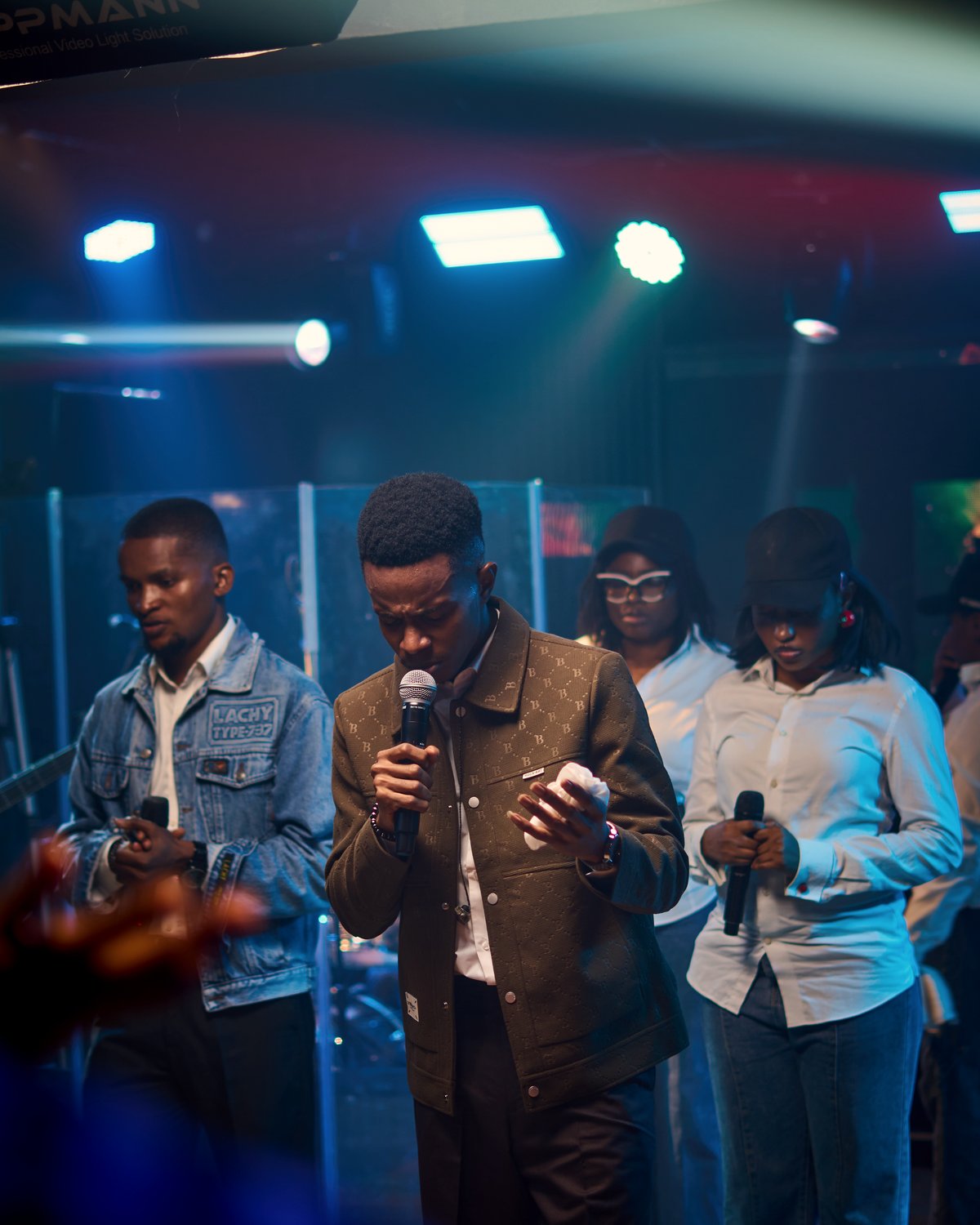 NWELL singing with his head bowed, the choir behind him.