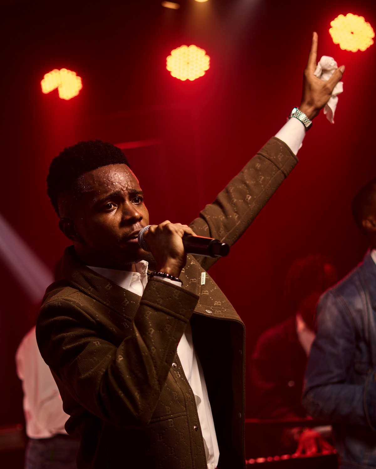 NWELL singing with one arm raised under red stage light.